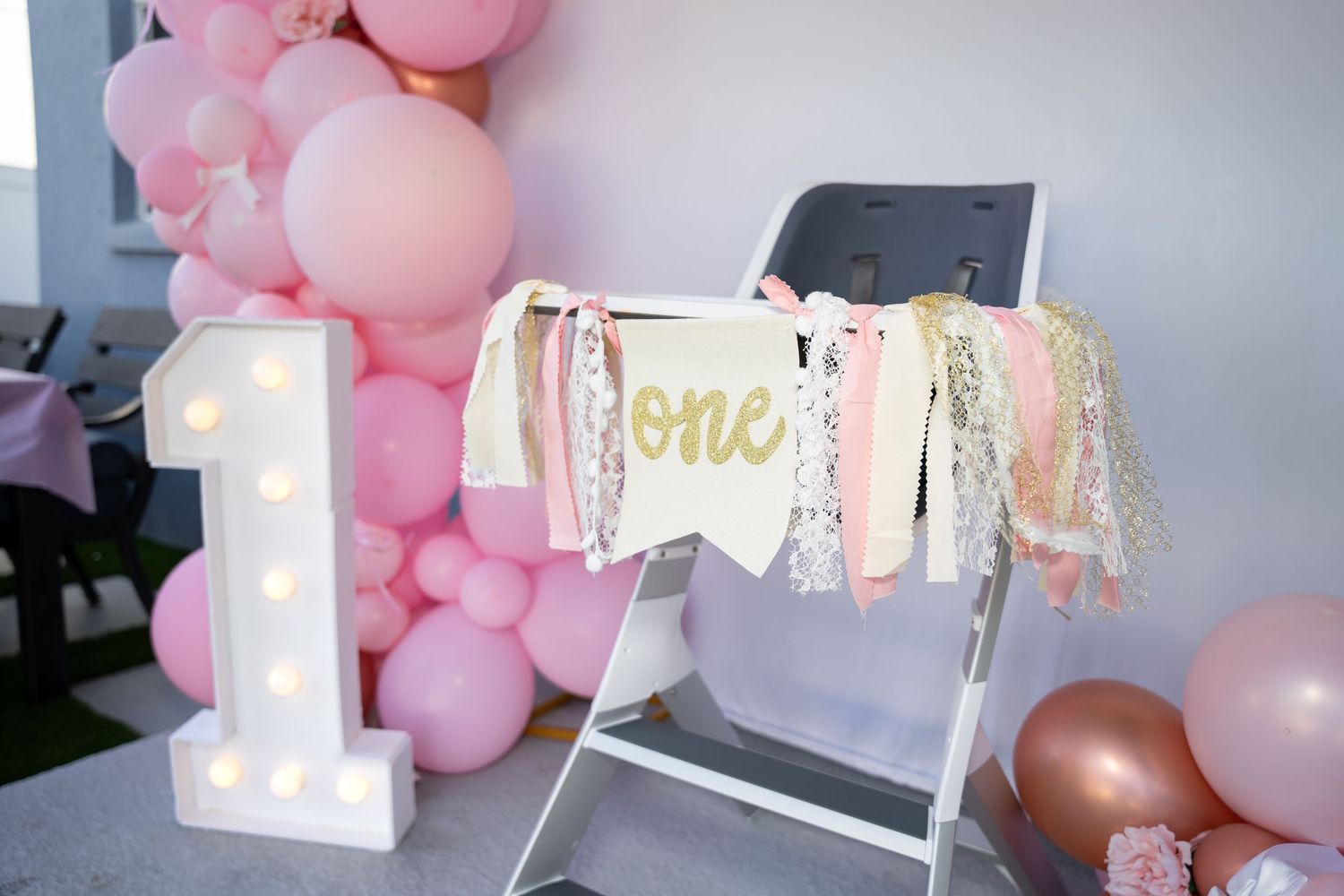First birthday party decoration with illuminated number one and pink balloon arch.