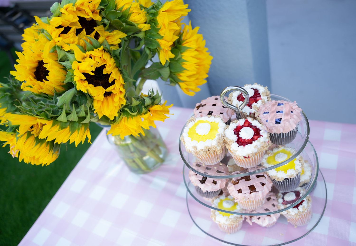 Tiered serving plate of decorated cookies next to vibrant sunflower bouquet.