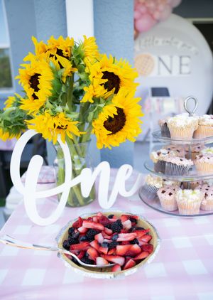 Party dessert table with sunflower centerpiece, fresh berries, and decorative signs.