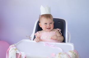 Baby in high chair at birthday celebration with decorative background.