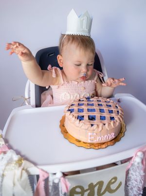Baby in high chair reaching for decorated birthday cake on tray.