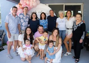 Large family gathering posed together on porch steps with pink balloon decorations.