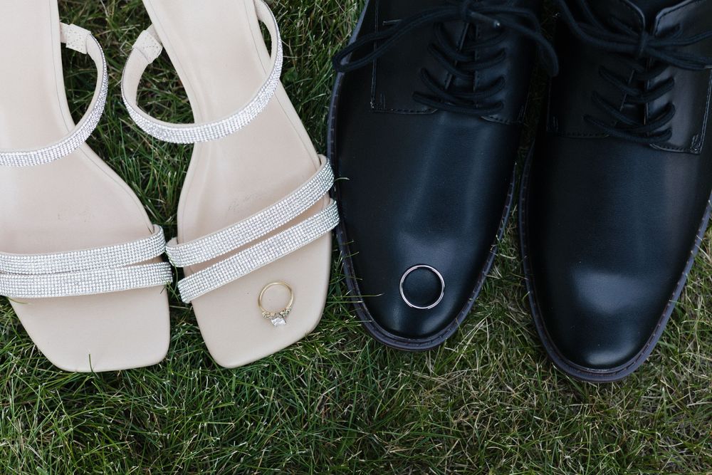 Black dress shoes and white sandals arranged in a row on green grass.