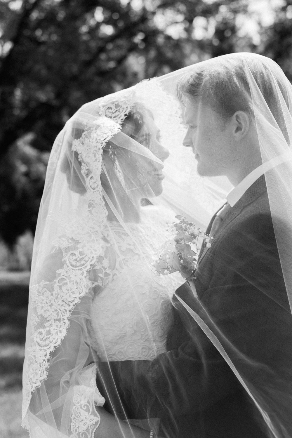Romantic black and white portrait of couple beneath delicate lace veil.