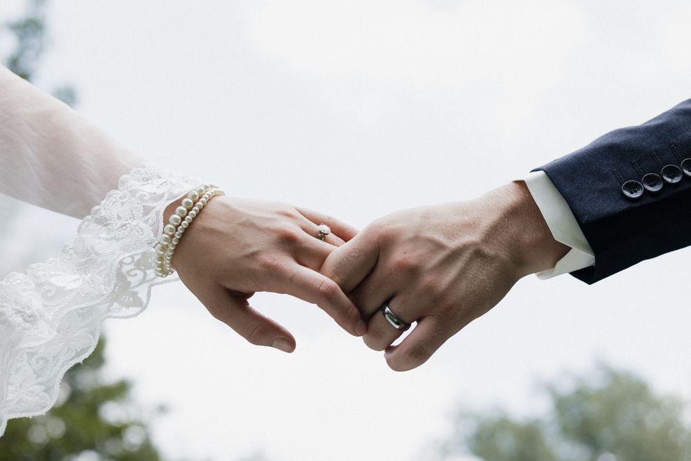 Close up shot of newlywed hands with wedding rings against a blurred outdoor background.