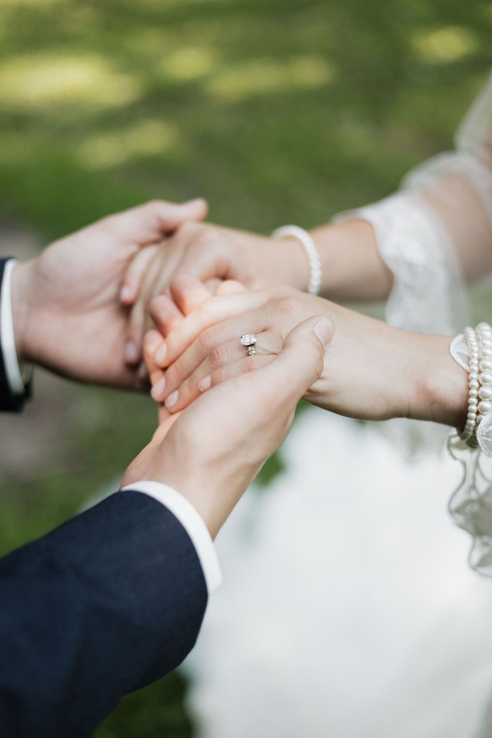 Close-up of hands with wedding ring and bracelets clasped together outdoors.