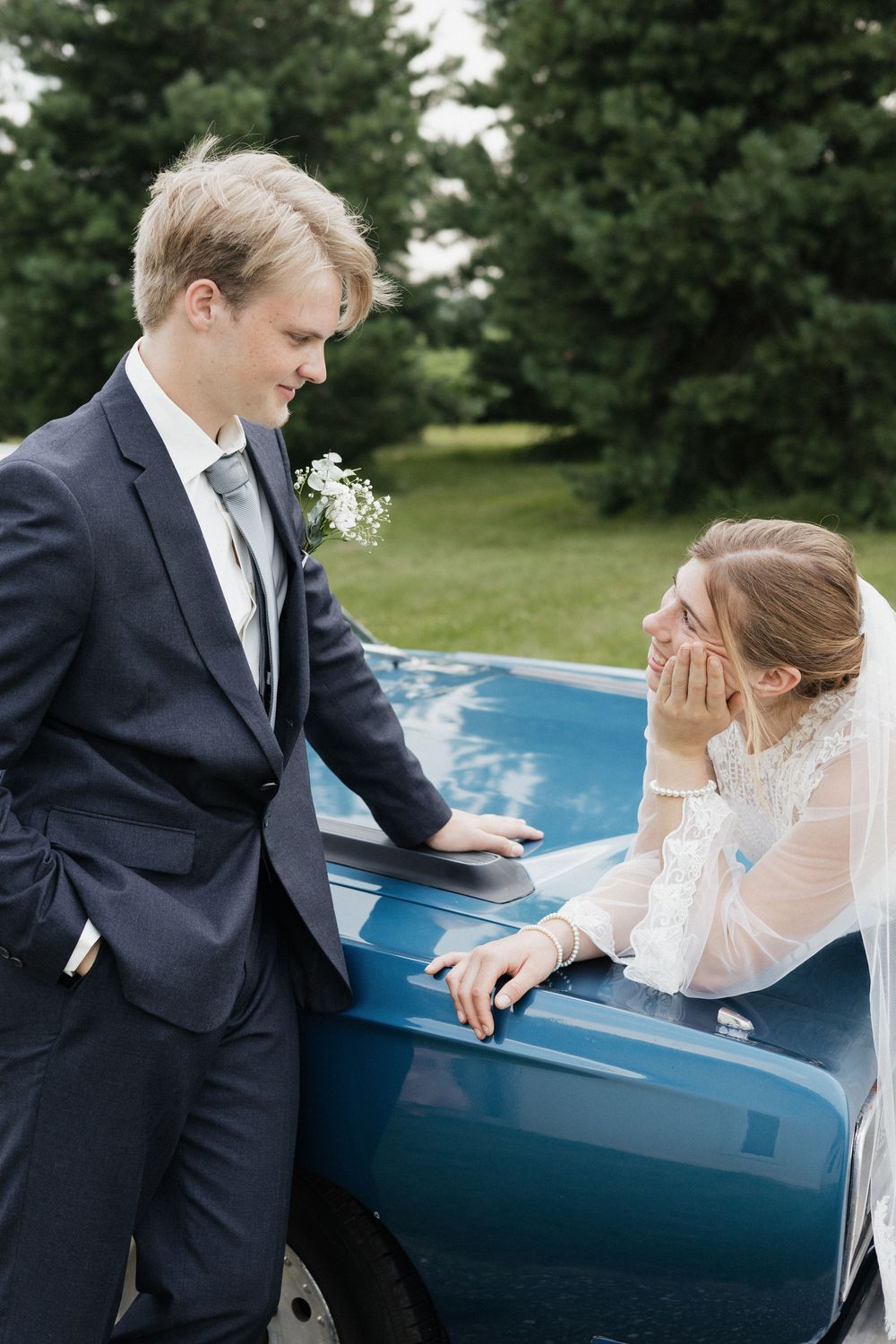 A candid moment between a couple by a vintage car during their wedding photoshoot outdoors.
