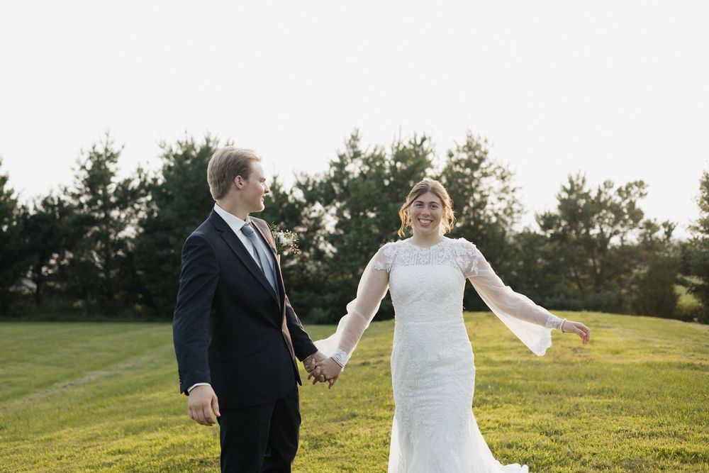 A couple holding hands while walking together on a grassy hillside during their wedding day.