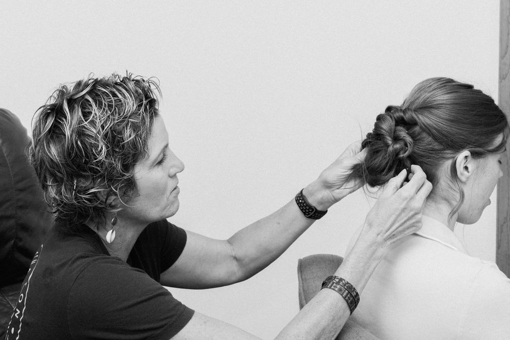 A professional hairstylist works on styling and pinning up a client's hair in black and white.