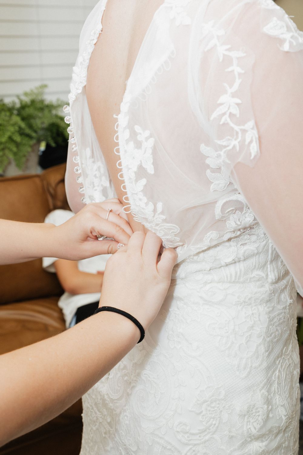 Close-up detail of intricate lace on a white wedding dress being fastened.