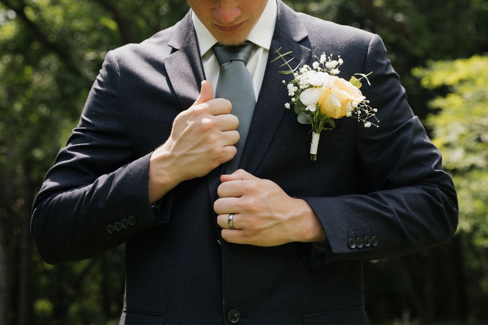 Groom adjusts tie while wearing black suit with yellow rose boutonniere.