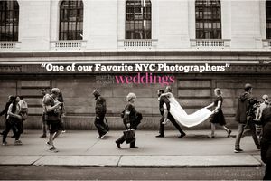 A creative black and white wedding photo on a city sidewalk with a flowing veil and walking pedestrians.