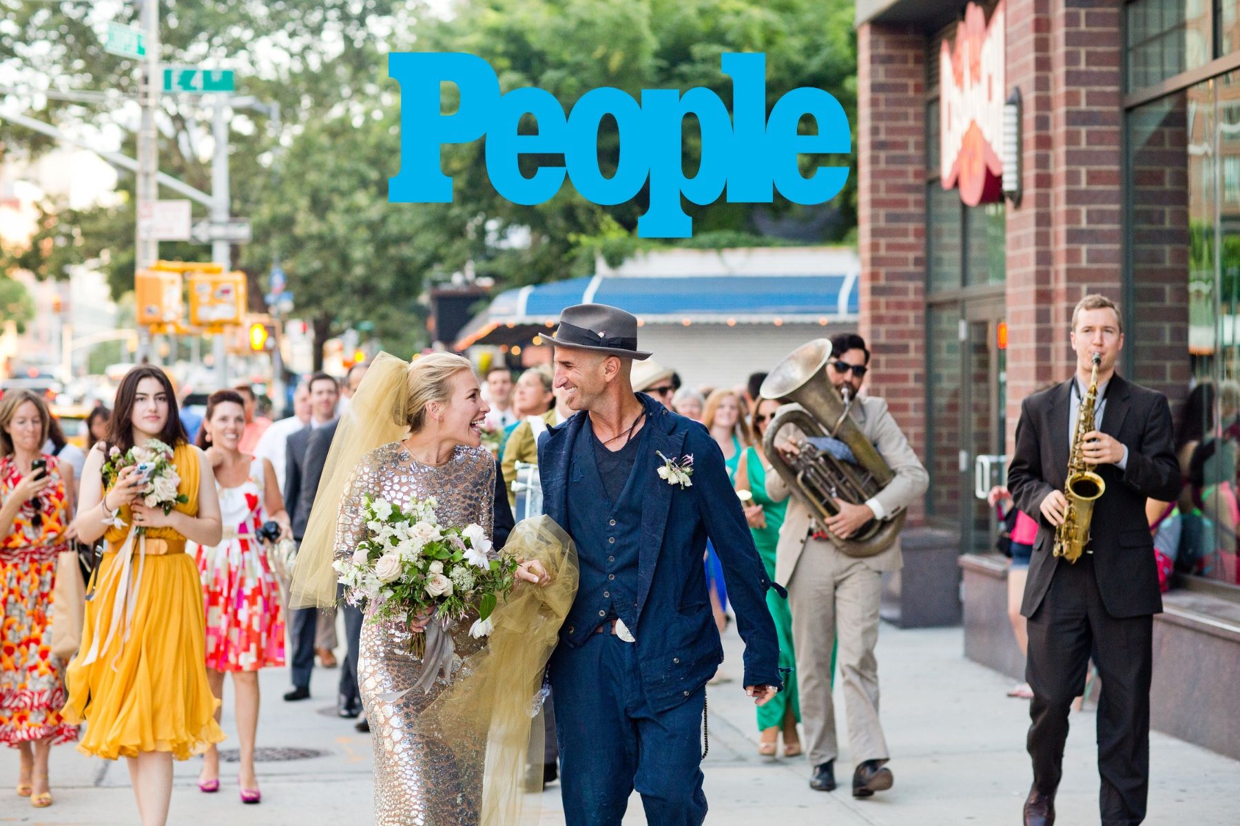A wedding procession walking down a city street with musicians playing instruments in the background.