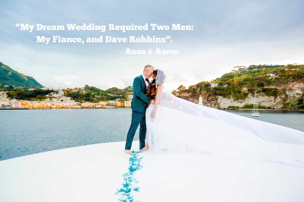 A wedding photo overlooking a scenic coastal bay with blue water and mountain backdrop.