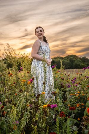 Person in floral dress walking through wildflower field during golden hour.