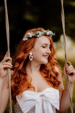 Woman on swing wearing flower crown and white dress with bow detail.