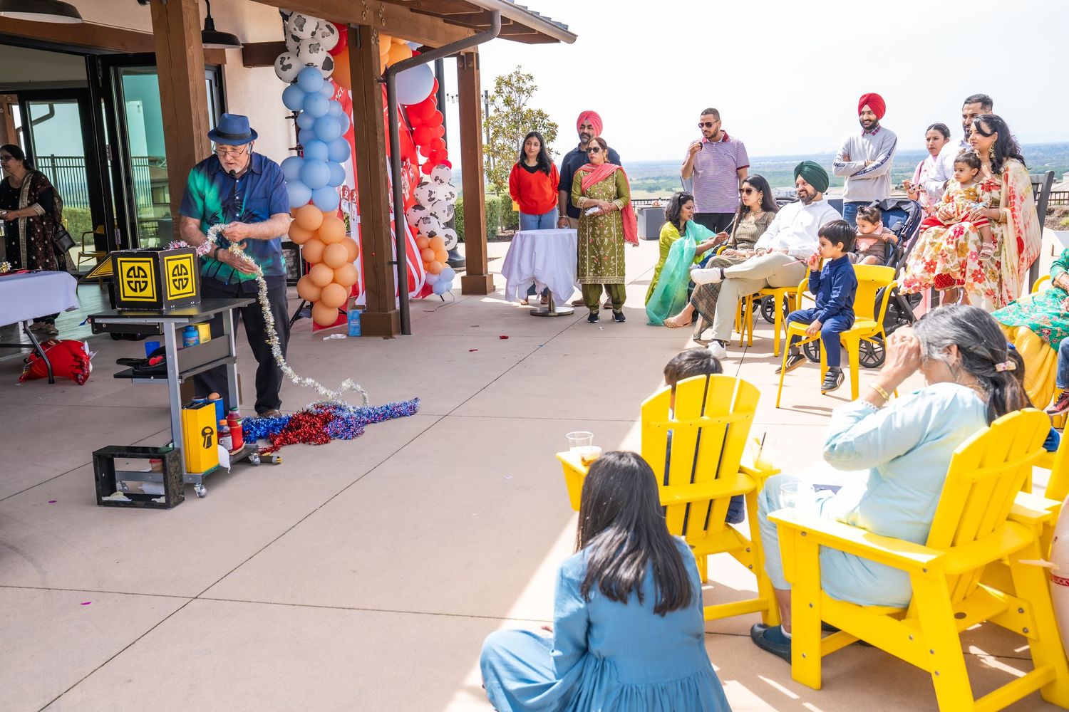 People sitting in colorful yellow Adirondack chairs at an outdoor walkway near shops and market stalls.