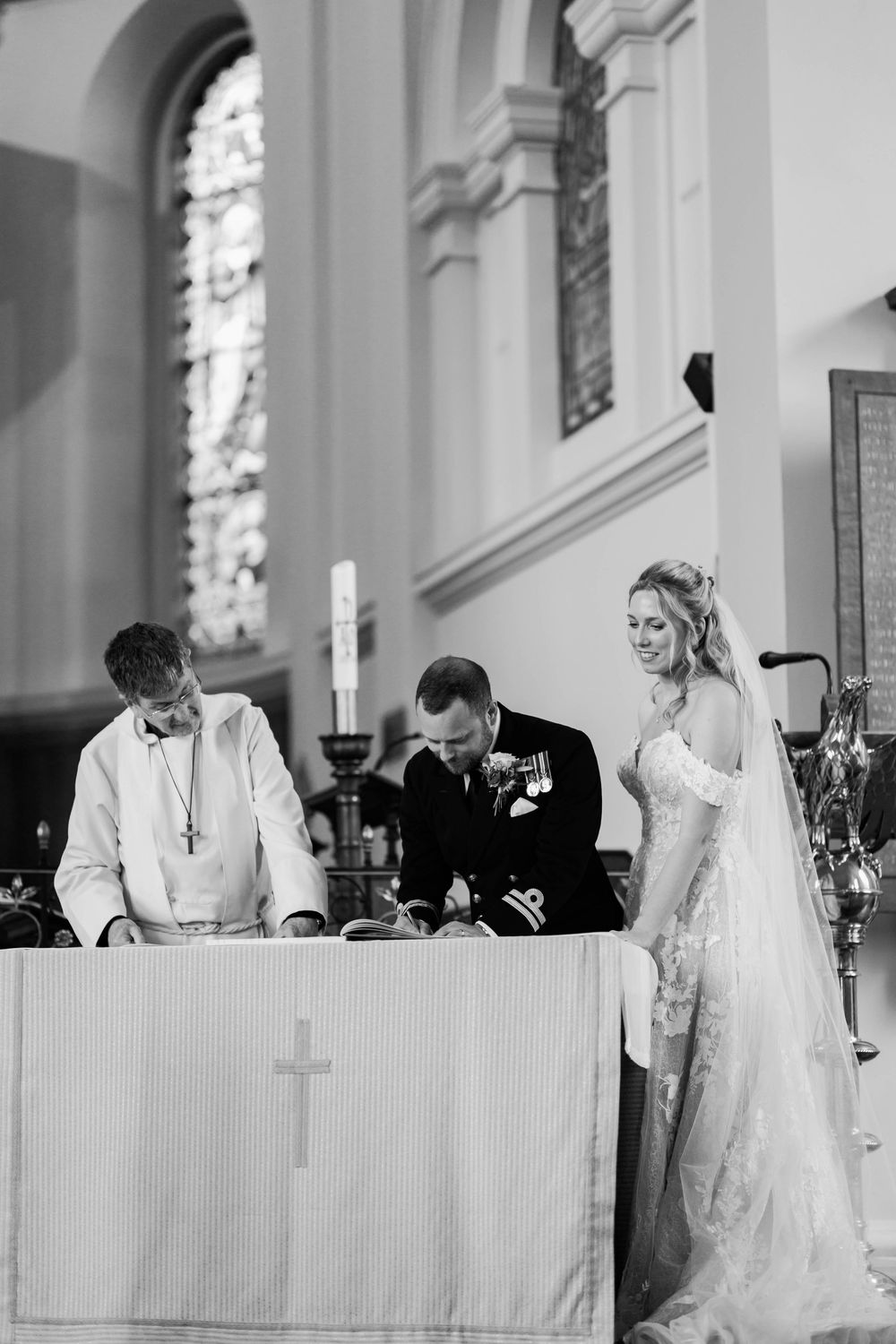 Black and white photo sequence showing wedding ceremony signing moments at an elegant church altar with stained glass windows.