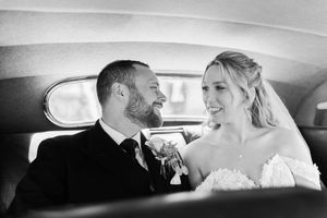 Two happy people share an intimate moment in the backseat of a vintage car during a wedding celebration.