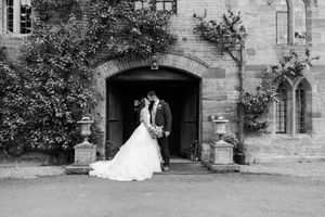 A couple poses together in a romantic wedding moment at a historic stone building with elegant archways.