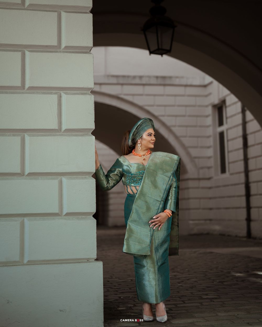 Person in an elegant mint green sari and matching outfit poses dramatically against a white stone archway.