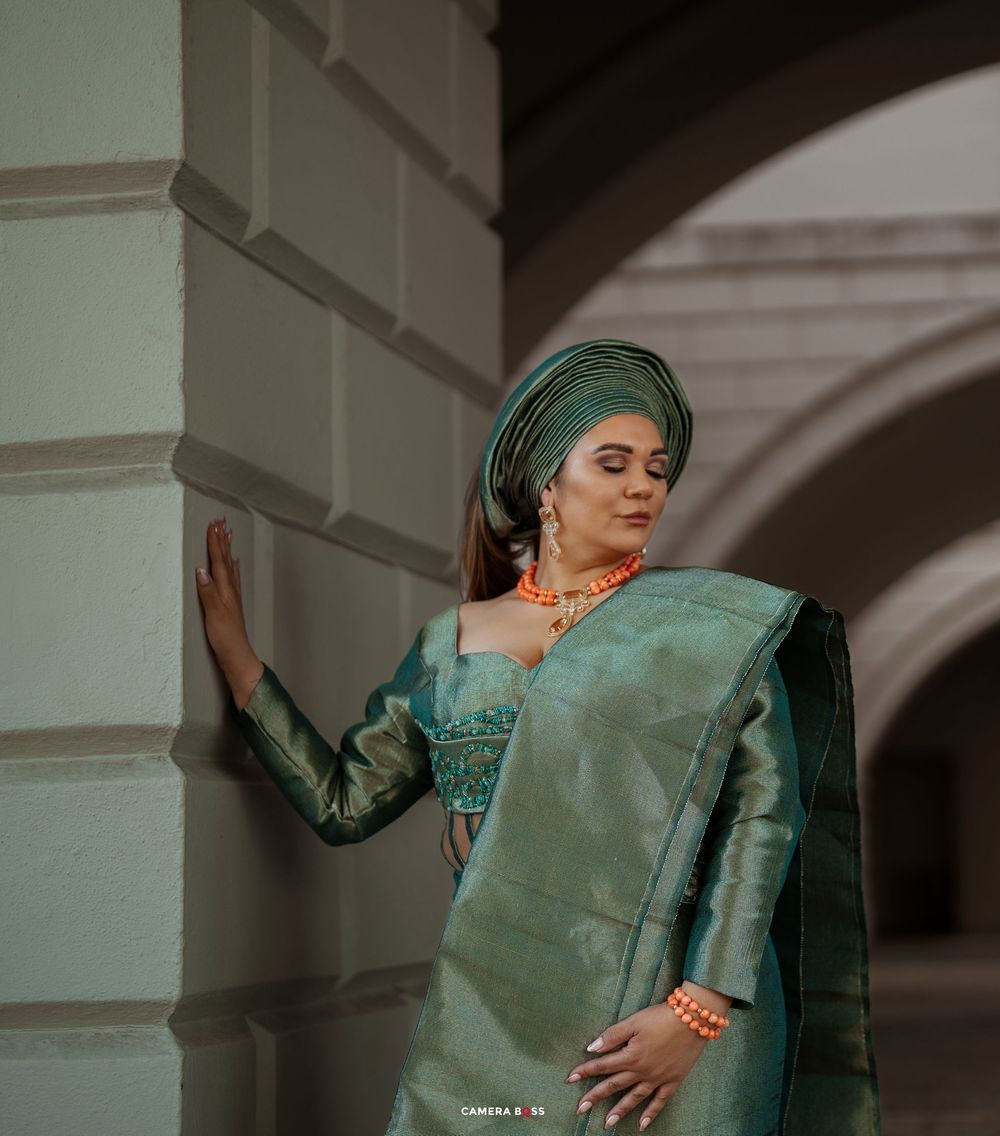 Woman in emerald green headscarf and dress poses gracefully against architectural backdrop in moody lighting.