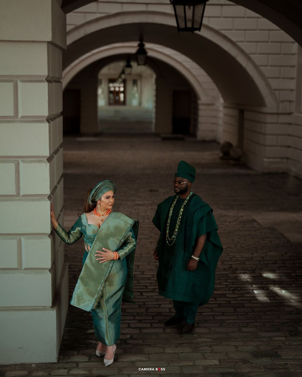 A couple in vintage outfits dances playfully under arched stone architecture in a romantic scene.