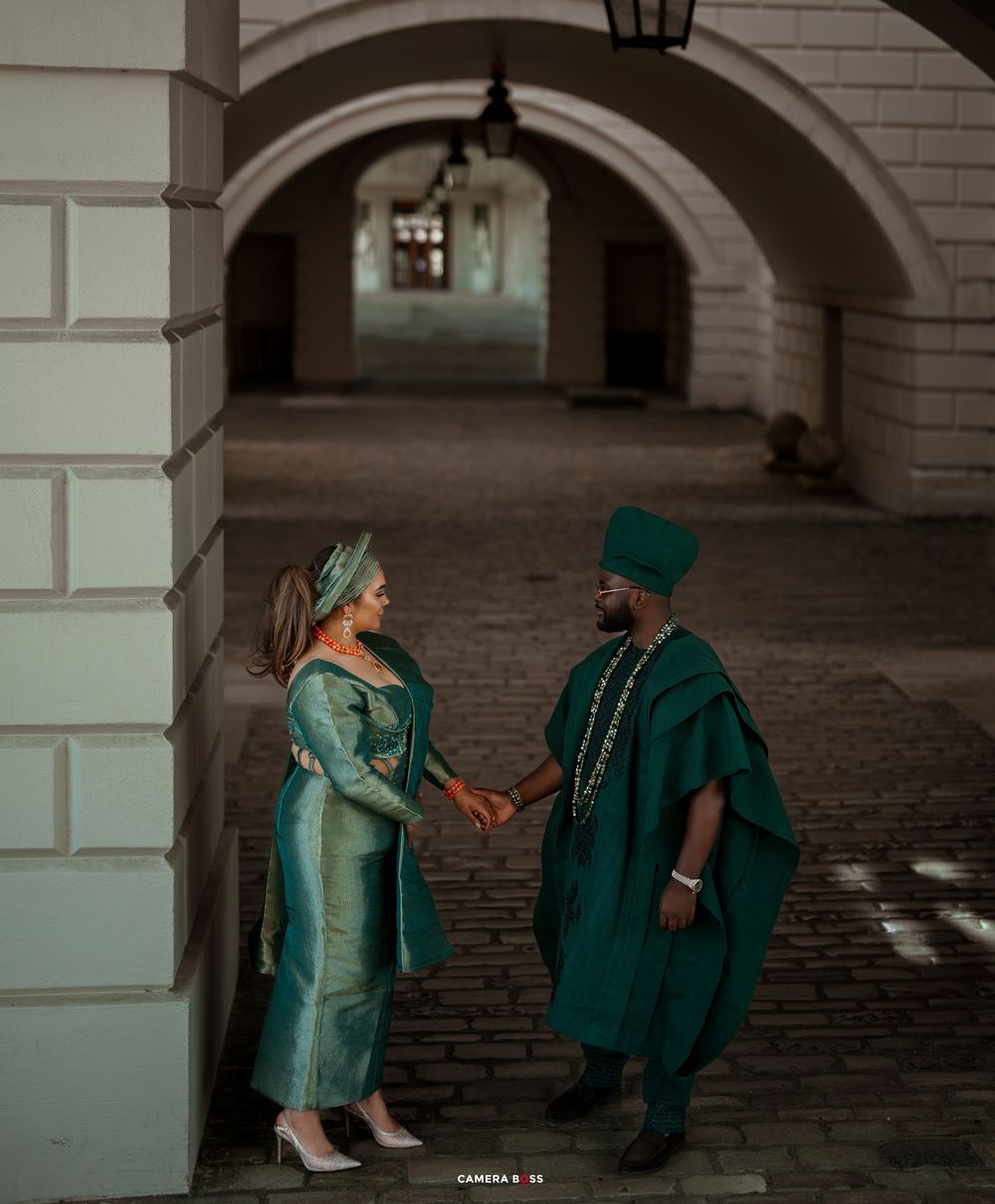A couple in elegant matching green outfits pose together under stone archways for romantic photos.