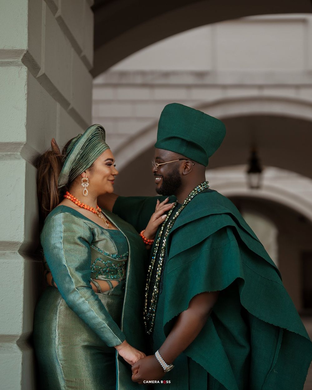 Romantic couple in coordinated green attire share an intimate moment under an arched colonnade.