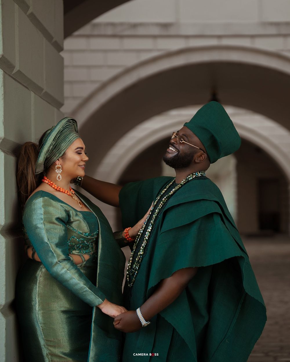A dramatic photoshoot featuring elegant green traditional formal wear against an arched architectural backdrop.