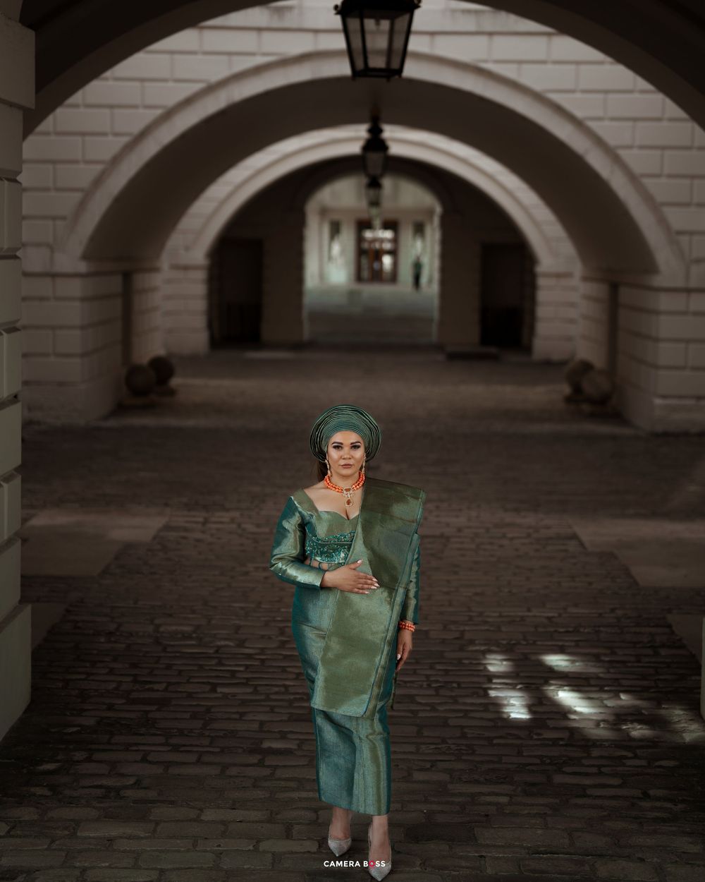 A person in a shimmering turquoise dress poses gracefully beneath a series of stone archways.