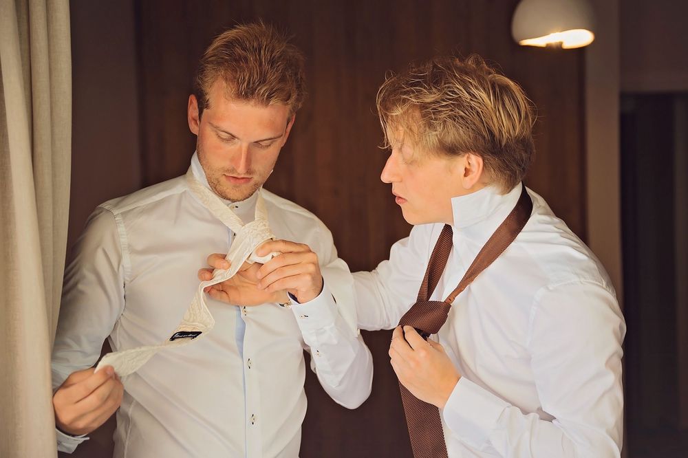 Indoor scene showing people adjusting formal attire in warm lighting.