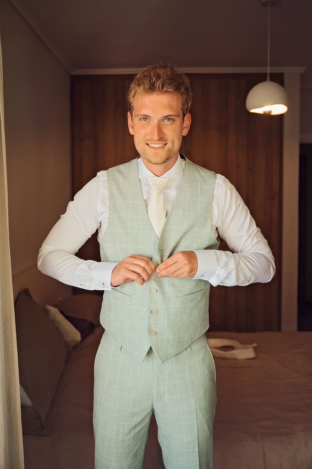 Person in mint green vest and white shirt getting dressed indoors.