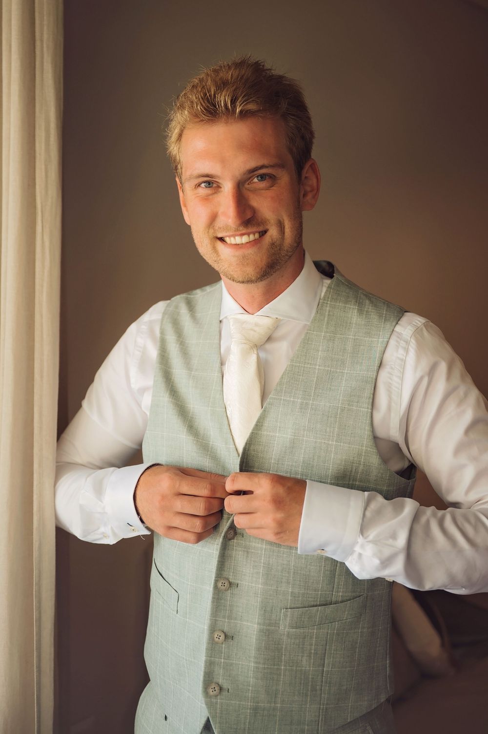 A light mint green vest being adjusted against a neutral background in preparation for a formal event.