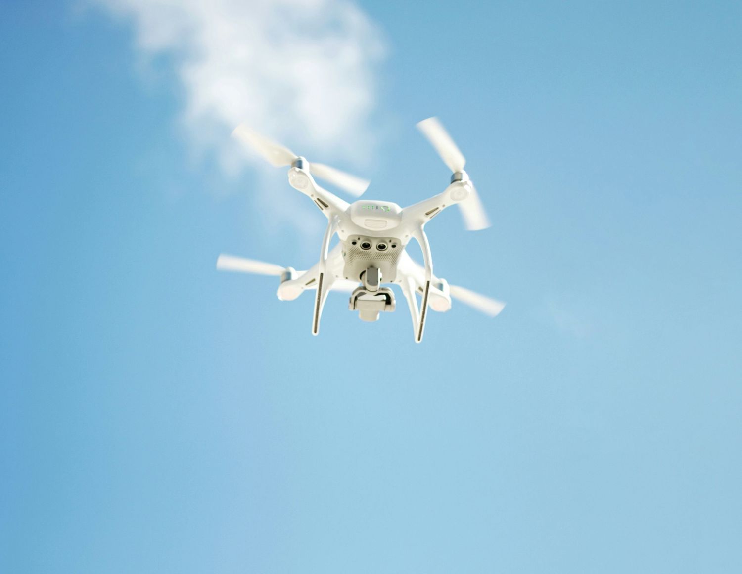 A white quadcopter drone flying against a bright blue sky background during daytime.