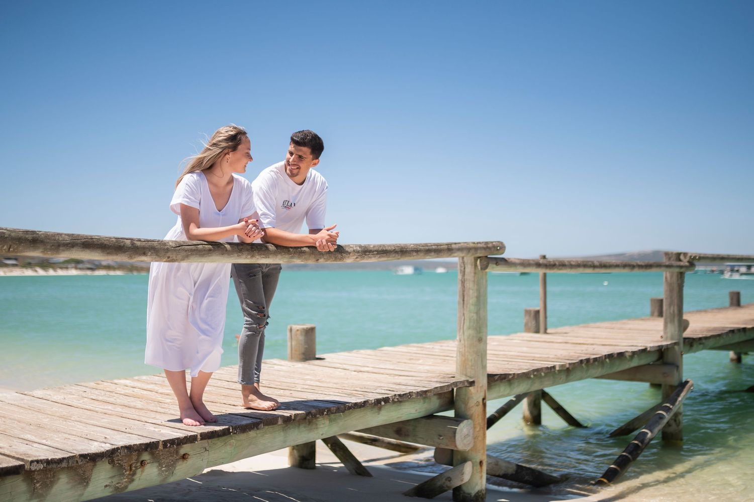 Couple enjoys romantic moment together on a wooden pier overlooking turquoise tropical waters at sunset.