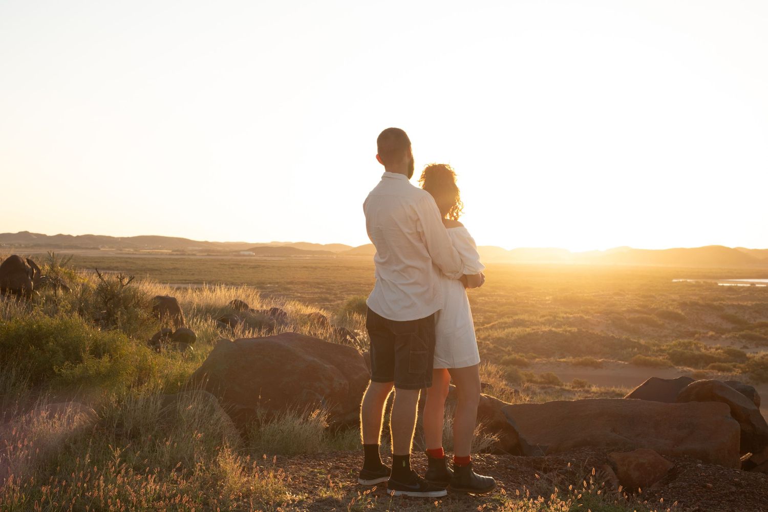 Silhouetted figures sit peacefully on hilltop during golden sunset.