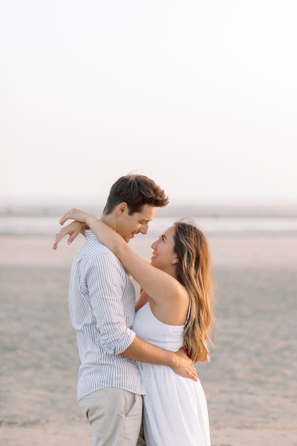 Intimate moment captured on empty beach with soft lighting and neutral tones.