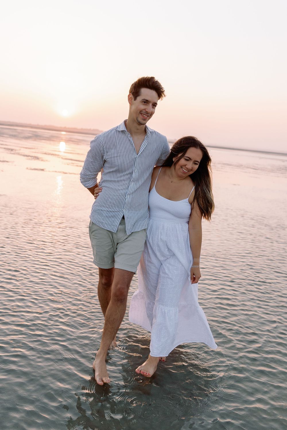 Happy couple wading together in shallow ocean water during sunset.