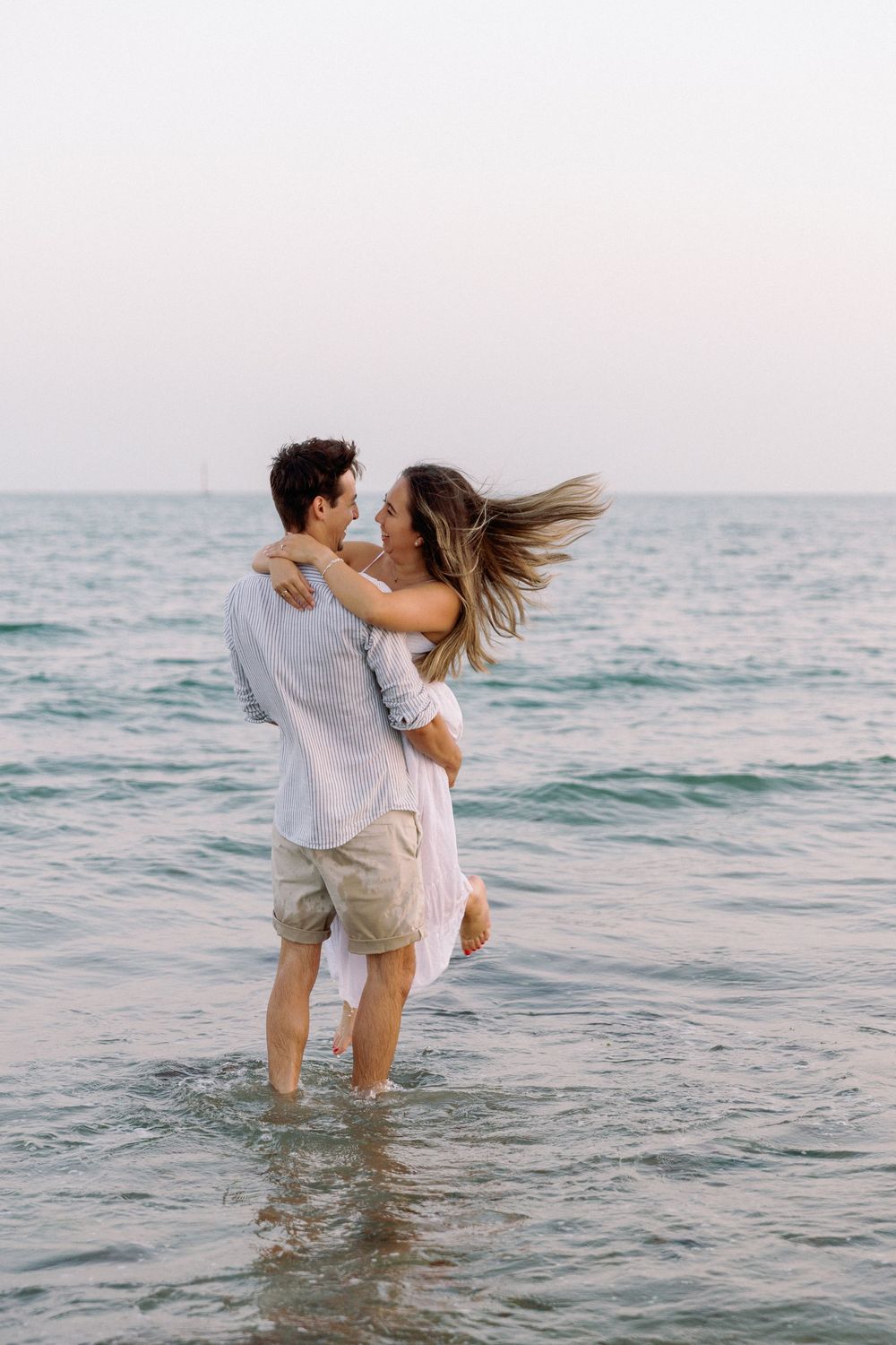 Playful couple wading in shallow ocean water as waves roll in during golden hour.
