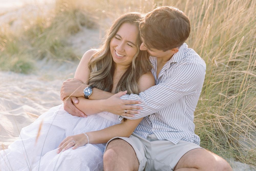 Intimate beach photoshoot with a couple in white and blue attire reclining on the sand.