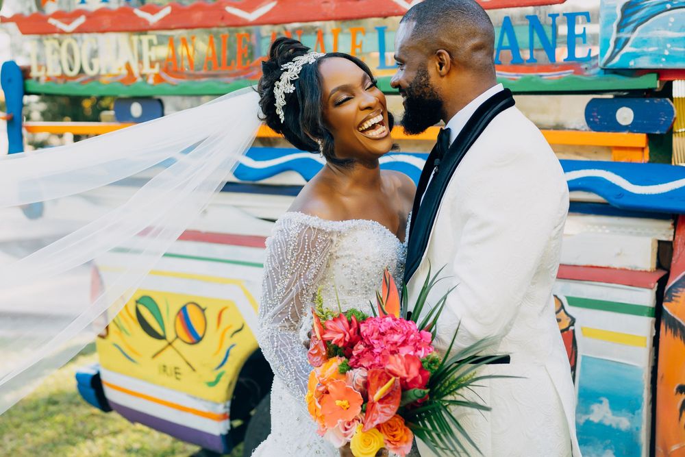 Joyful couple shares an intimate moment at a colorful fairground setting as a veil flows in the breeze with bright flowers.