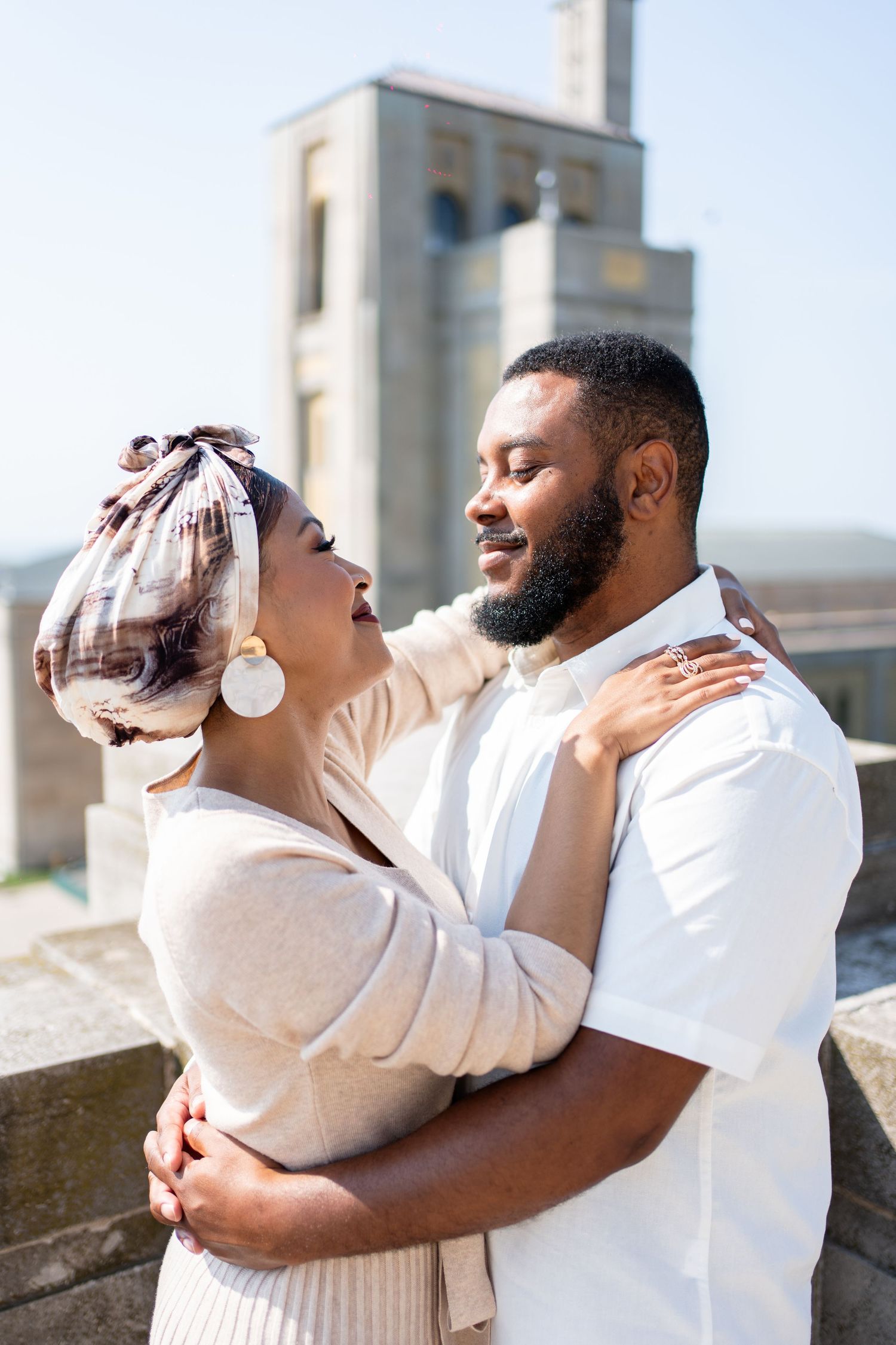 A couple in matching white outfits share an intimate moment on a sunny outdoor balcony.