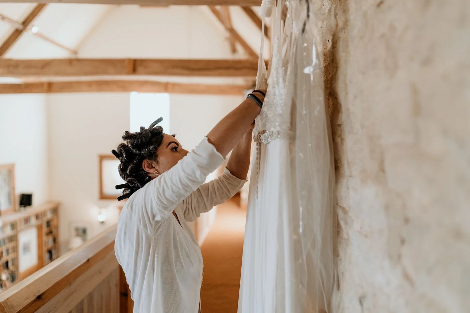 Women getting ready joyfully in a rustic bridal suite with white walls and exposed beams.