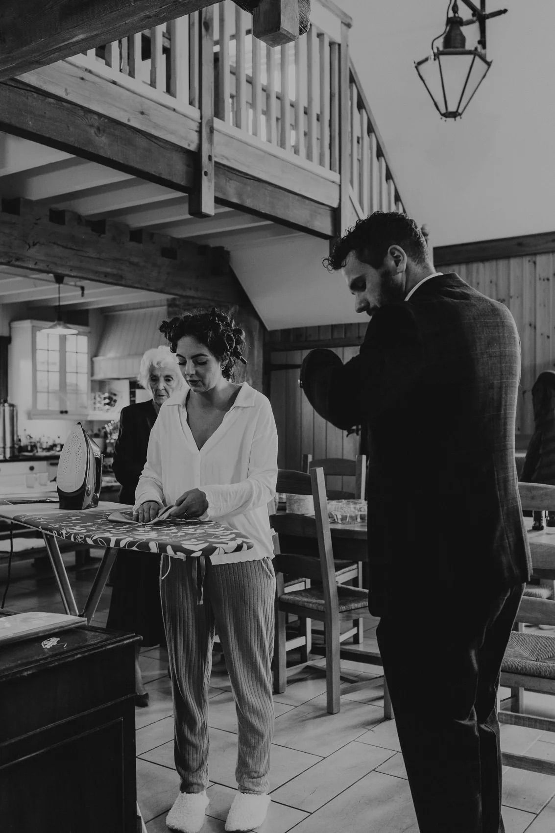 Black and white image showing wedding preparations in a rustic indoor setting.
