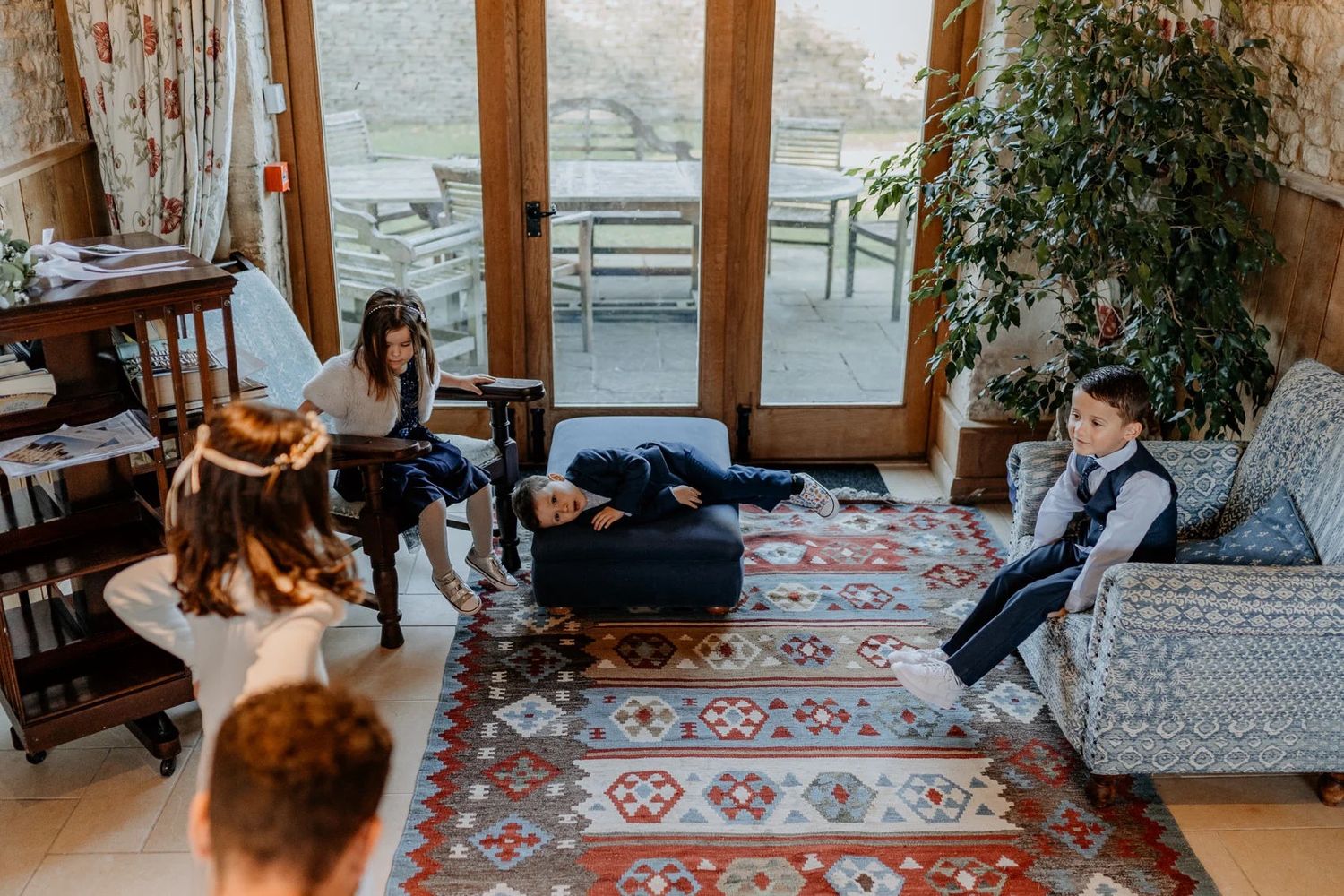 Wedding party relaxing on patterned rugs in a sunlit room with large windows.
