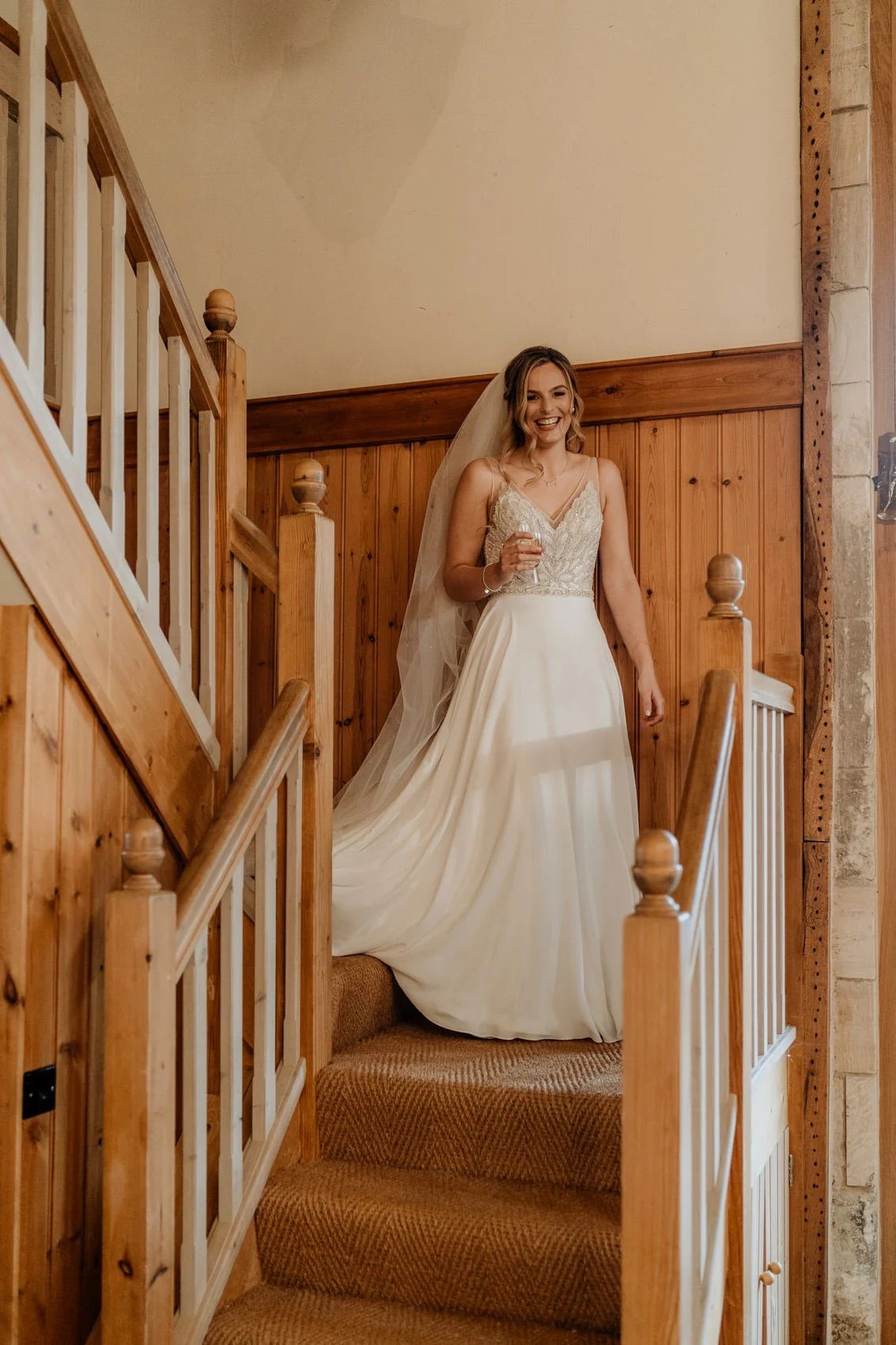 A white wedding dress flowing down wooden stairs with a carpeted runner in a rustic venue.