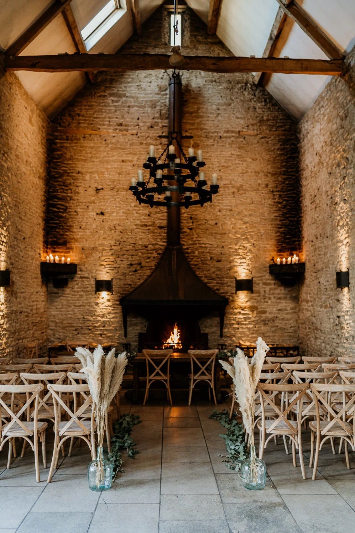 Rustic stone barn wedding venue with wooden chairs and chandeliers set up for ceremony.