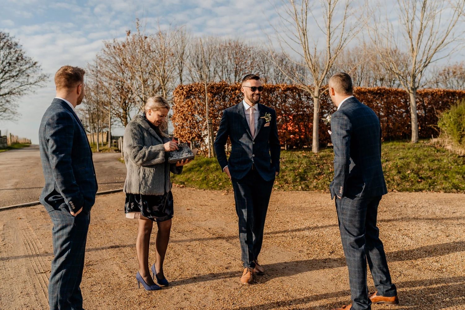 Several people gathered outdoors on a sunny day near bare trees in autumn or winter.