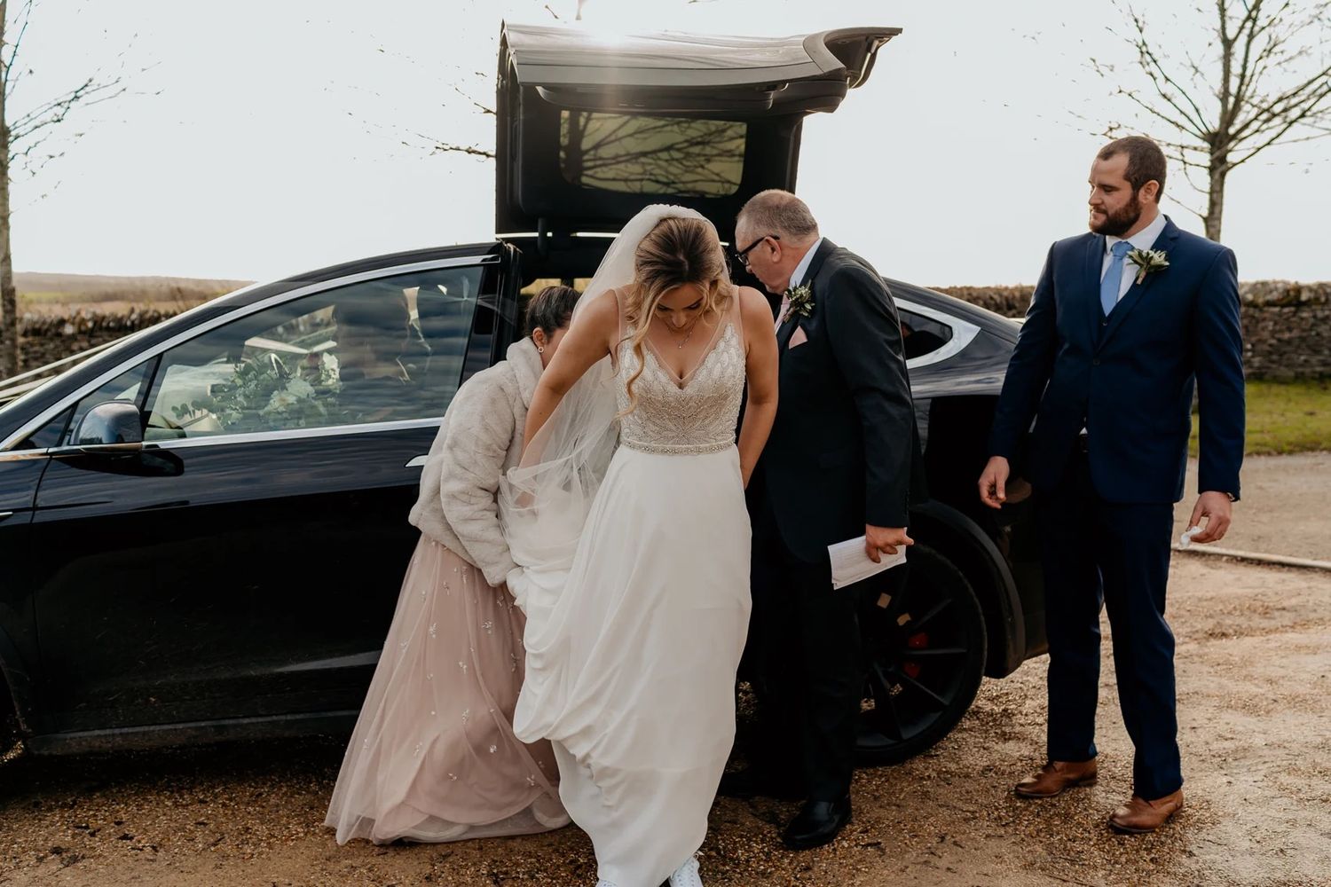 Candid wedding party moments captured outside with cars and trees in the background.